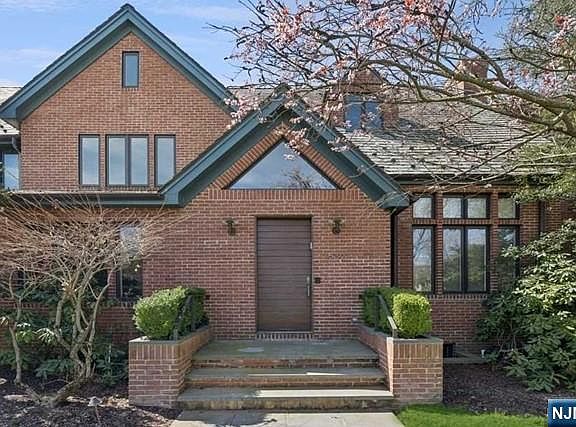 Close approach to the front door of 532 Winthrop, the brick gables and green trim filling the frame above a flagstone stoop with a flowering magnolia overhead