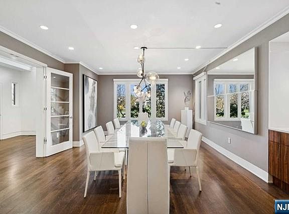 The formal dining room with a long white table set for ten beneath a contemporary bubble chandelier, dark hardwood floors, and large windows looking out to the property